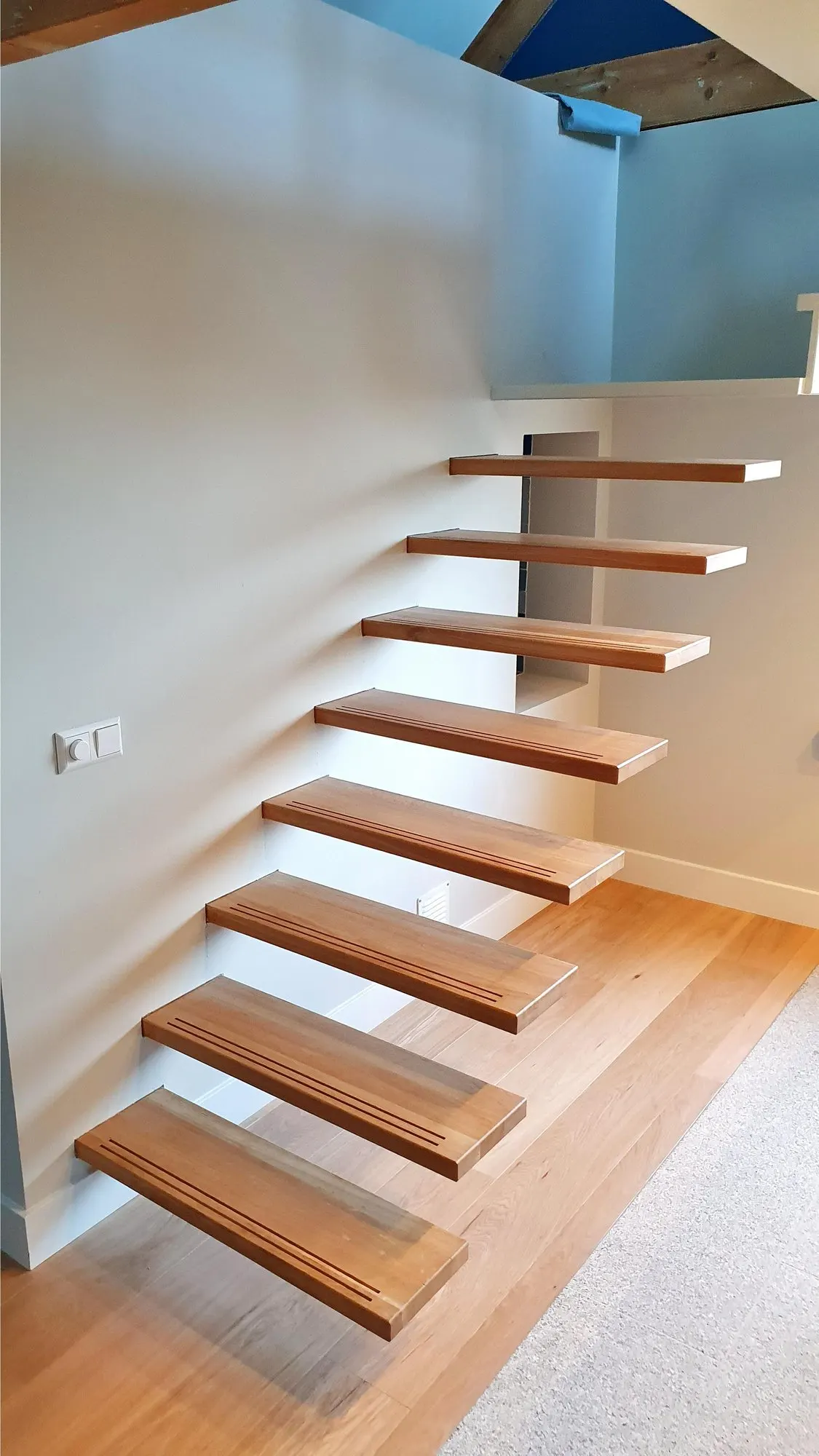Escalier suspendu aux marches en chêne massif fixées dans un mur blanc