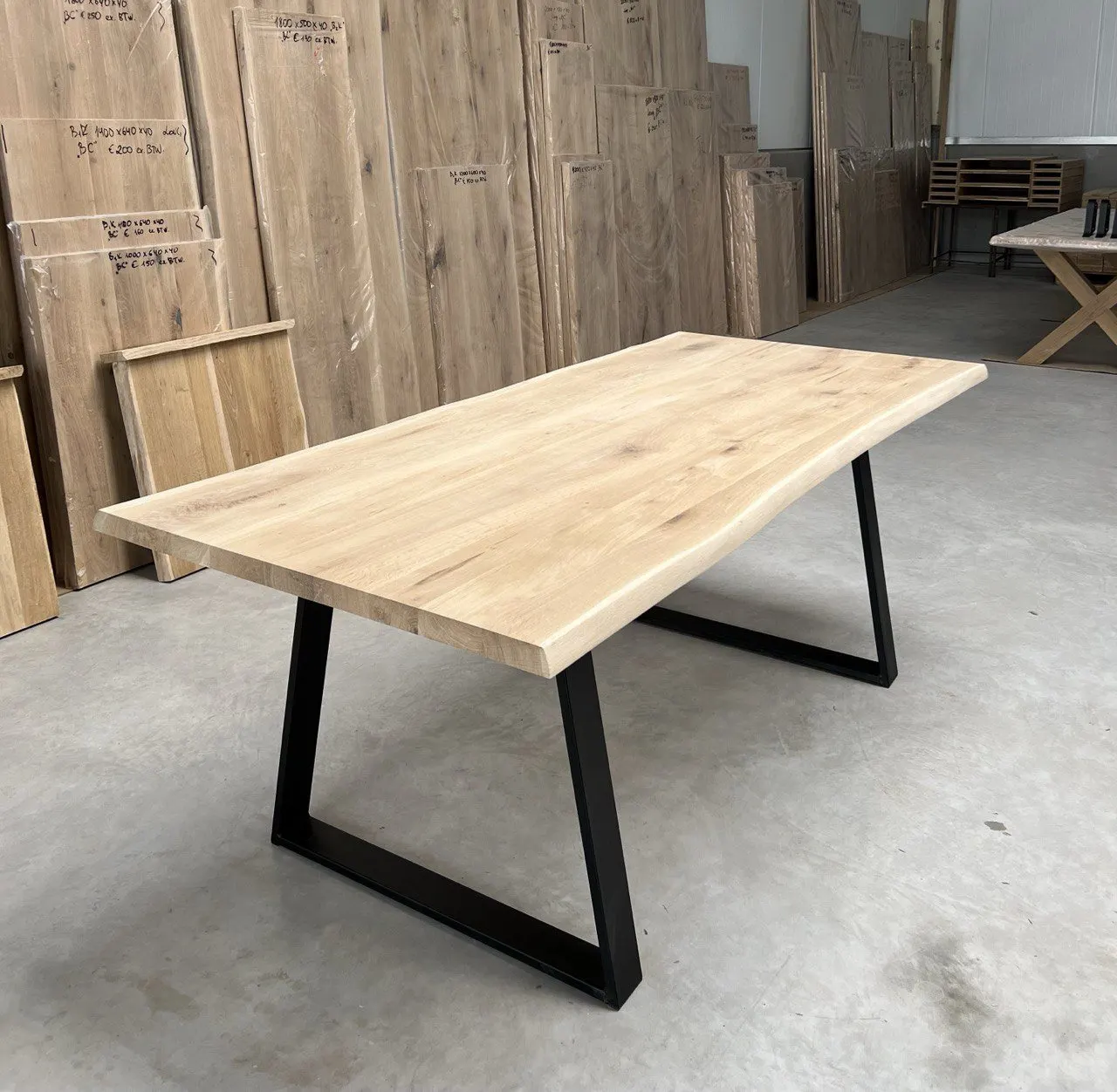 Plateau de table en chêne à bords naturels sur ses deux longueurs, posé sur un piètement noir au dépôt