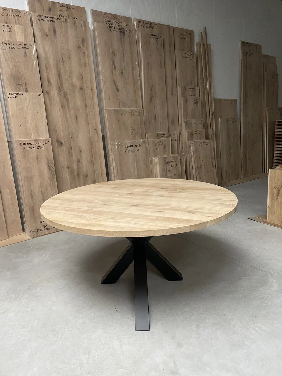 Plateau de table rond en chêne sur un piètement noir, au dépôt devant des planches de chêne